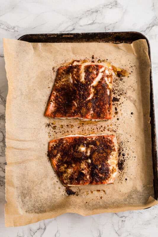 Two pieces of chipotle salmon on parchment paper baking sheet.