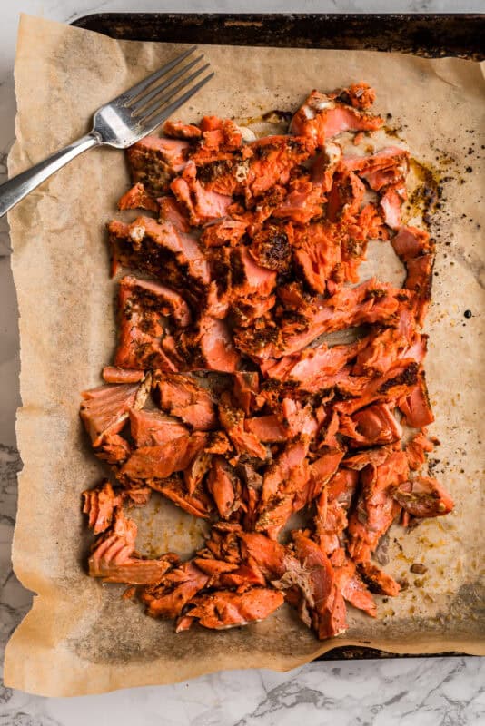Chipotle salmon flaked on a parchment paper lined baking sheet.