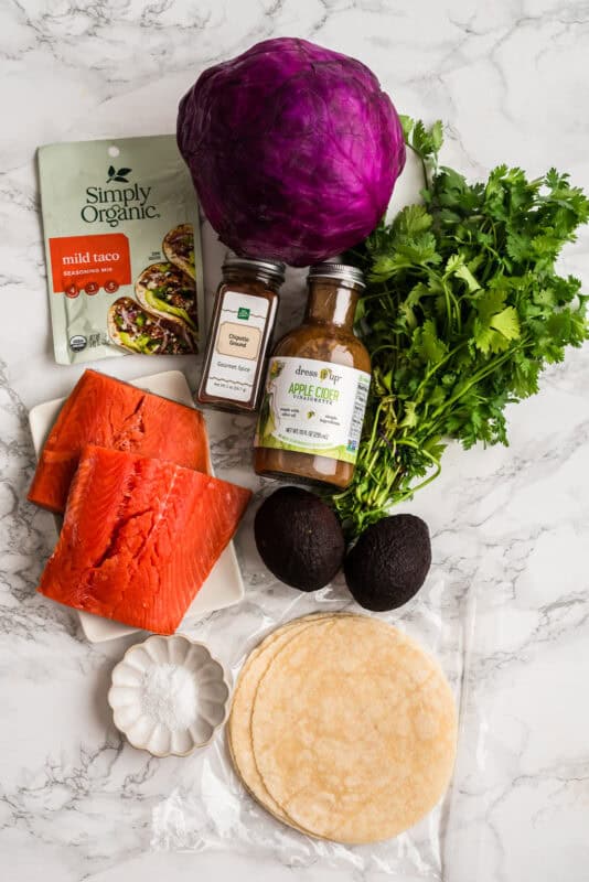 Ingredients to make chipotle salmon tacos on a marble countertop.
