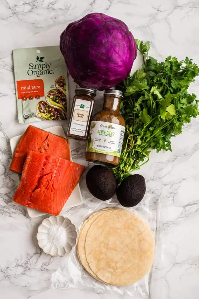 Ingredients to make chipotle salmon tacos on a marble countertop.