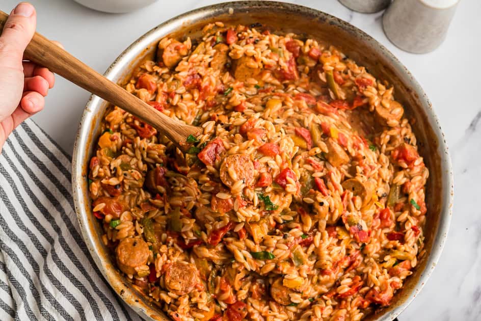 Cajun chicken sausage orzo being lifted out of the pan with a wood spoon.