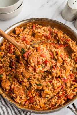 Cajun orzo with chicken sausage in a large skillet, some being lifted out of the pan with a wood spoon.