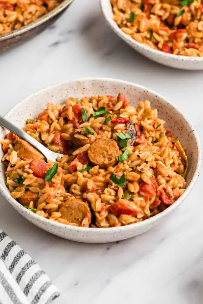 Cajun chicken orzo in a white bowl, fork resting in the bowl.