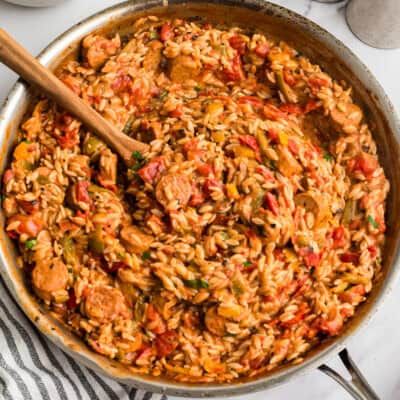 Large skillet filled with cajun chicken orzo with a wood spoon resting in the skillet.