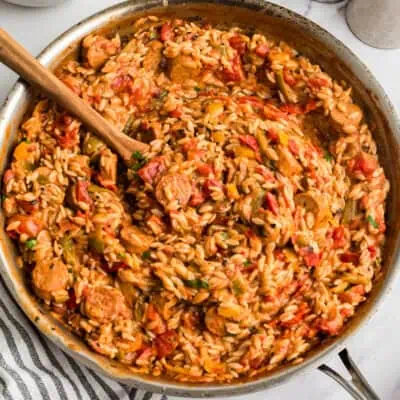 Large skillet filled with cajun chicken orzo with a wood spoon resting in the skillet.