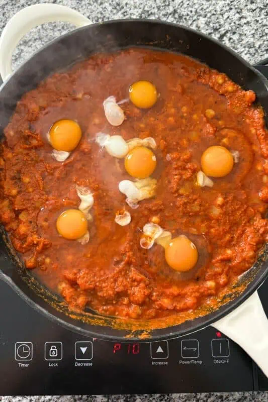 Six eggs cracked onto the tomato mixture in cast iron skillet.