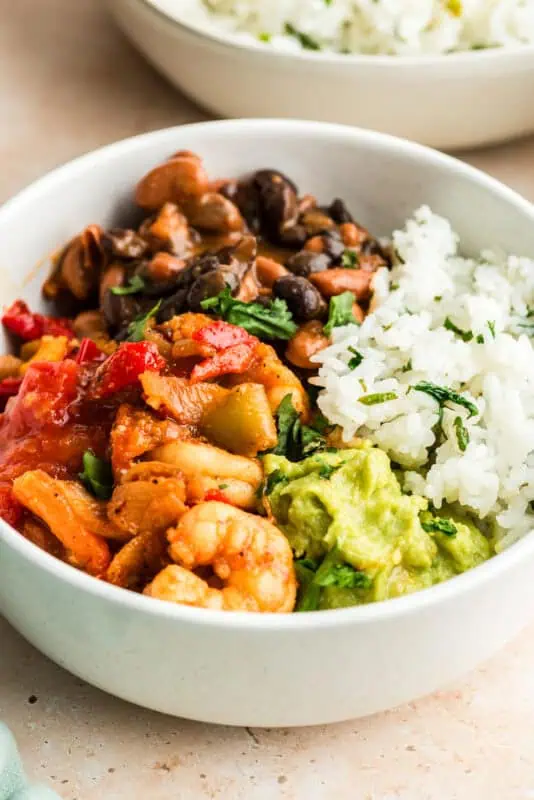 White bowl filled with shrimp, beans, rice and guacamole.