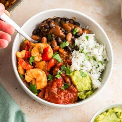 Hand holding fork resting in a shrimp burrito bowl.