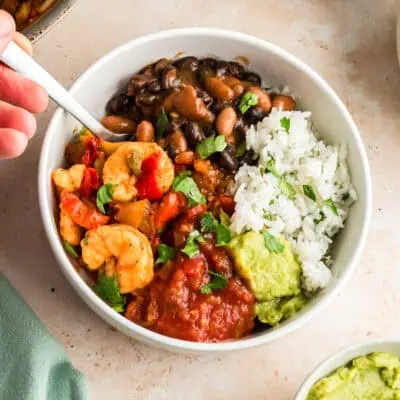 Hand holding fork resting in a shrimp burrito bowl.