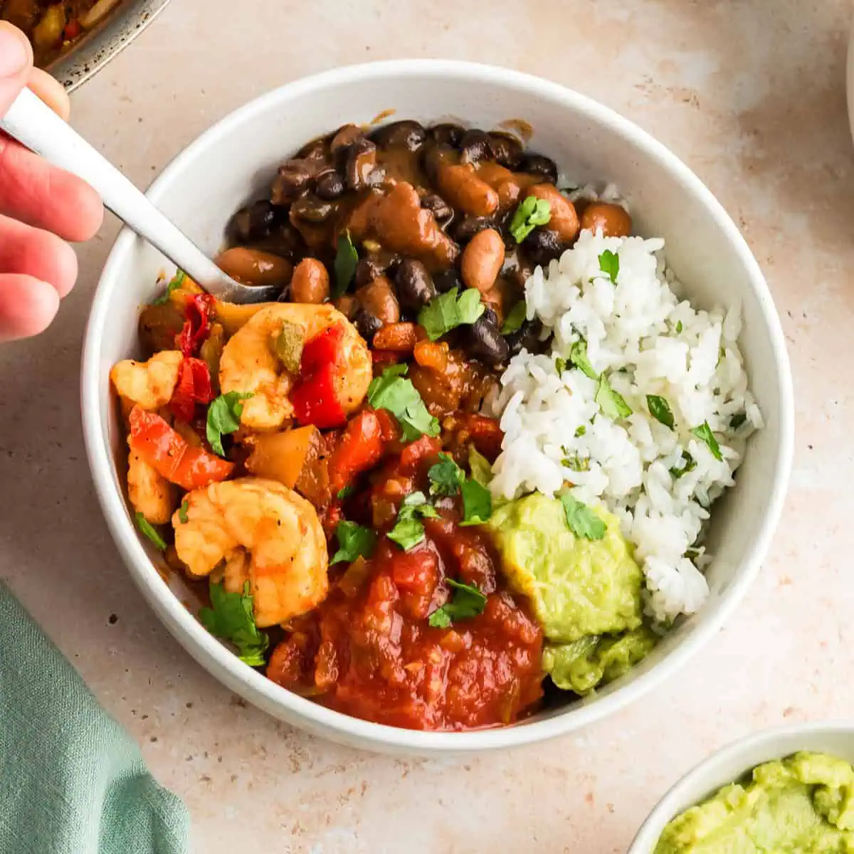 Hand holding a fork in a bowl filled with shrimp, beans and rice.