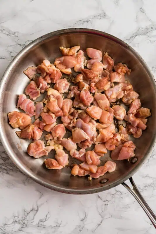 Raw chicken cut into cubes in stainless steel pan.