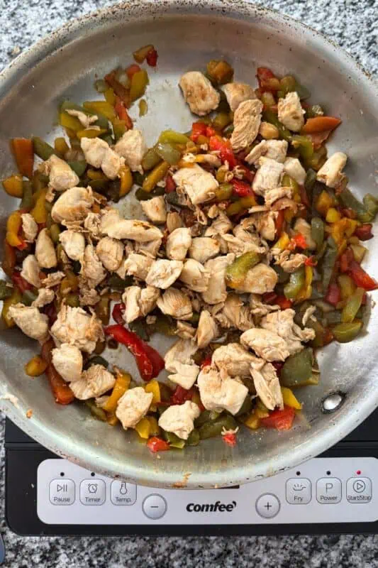 Cooked cubed chicken added to pan with veggies after cooking.