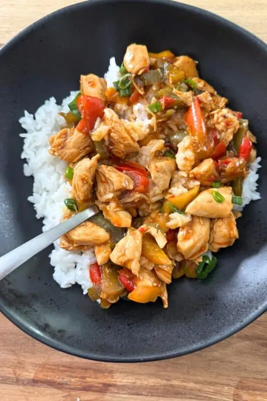 Sweet chili chicken served over cooked rice in a black bowl.