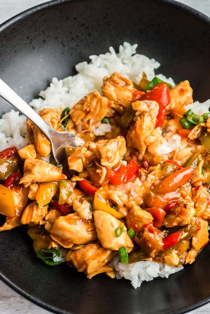 Fork resting in a bowl of sweet chili chicken and rice.