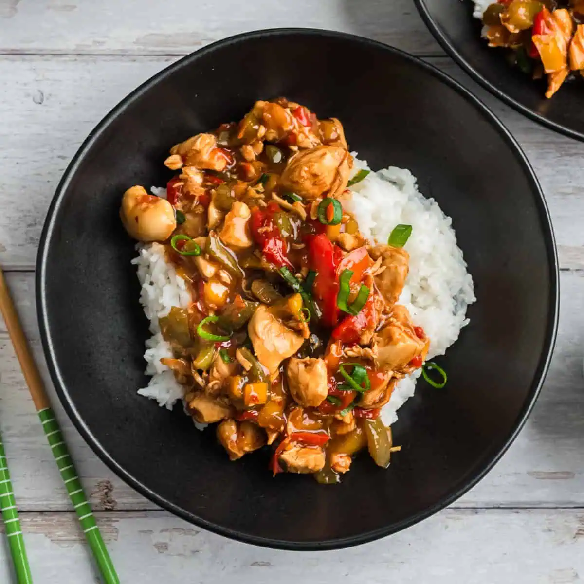 Sweet chili chicken and rice in a black bowl with chopsticks to the side.