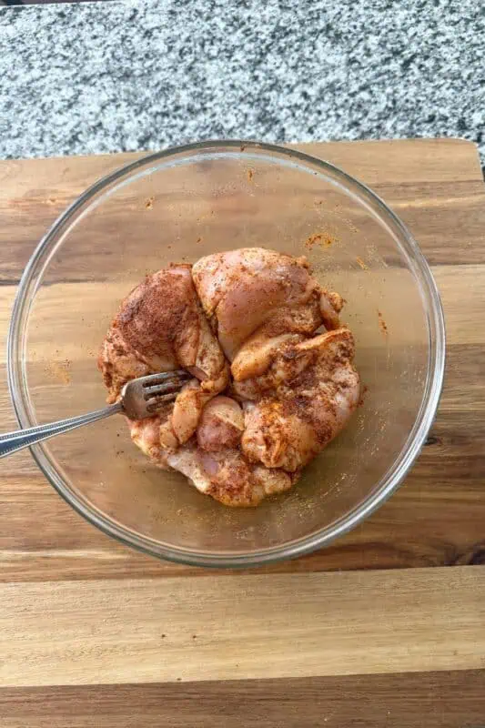 Chicken thighs coated in taco seasoning on glass bowl.