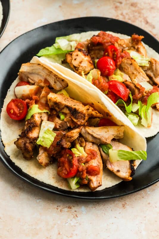 Two air fryer chicken tacos on a black plate.