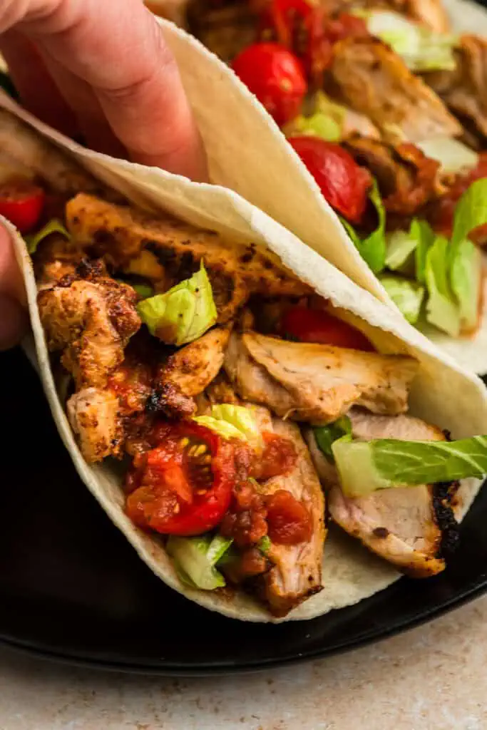 Hand picking up air fryer chicken taco off a plate.