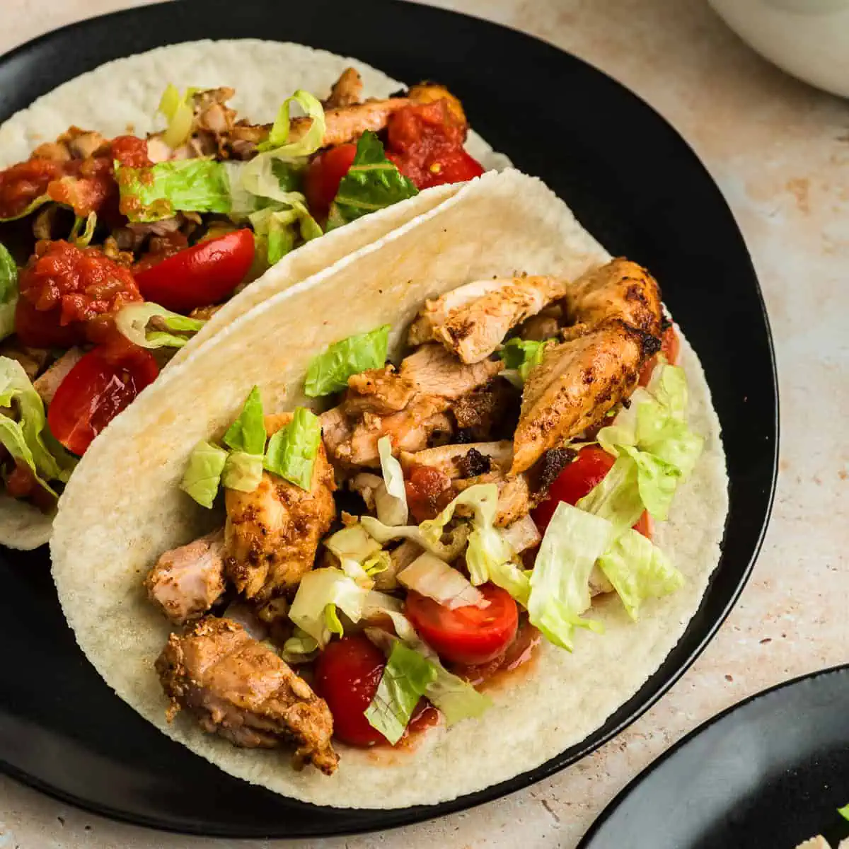 Air fryer chicken tacos with lettuce, tomato and salsa on black plate.