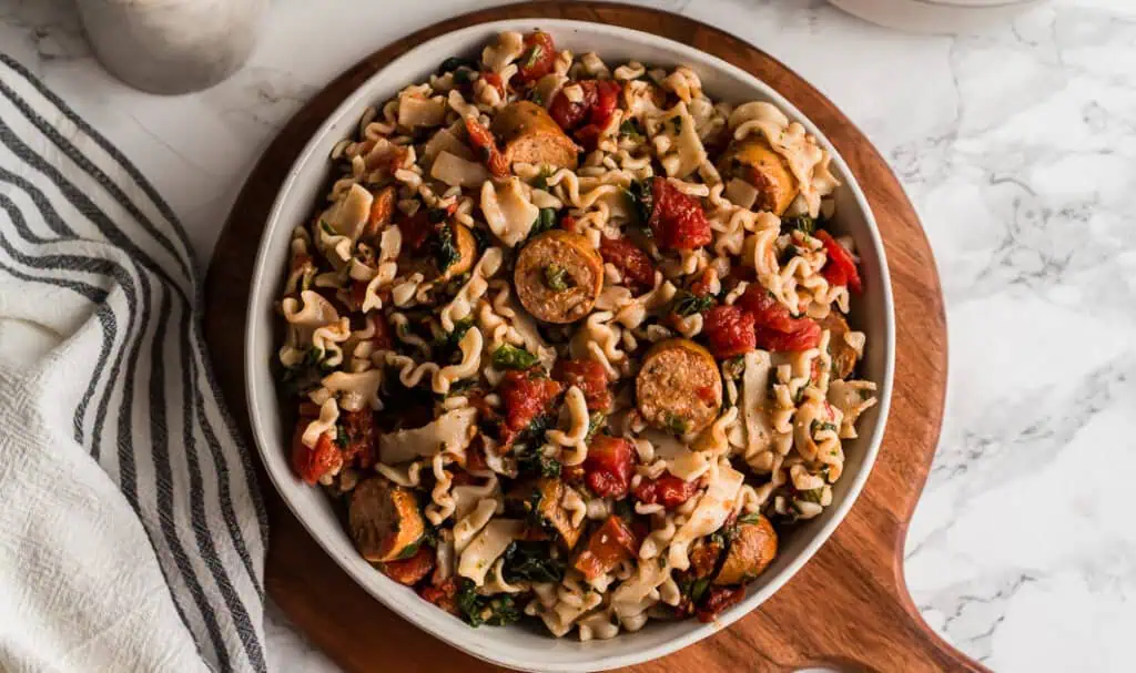Large bowl of italian chicken sausage pasta on a wood board. 