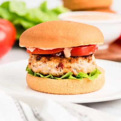 Chipotle chicken burger on white plate. Burger is on a bun and has lettuce, tomato and chipotle mayo on top.