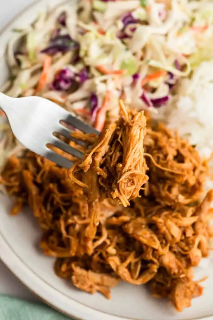 Forkful of shredded bbq chicken being held over plate.