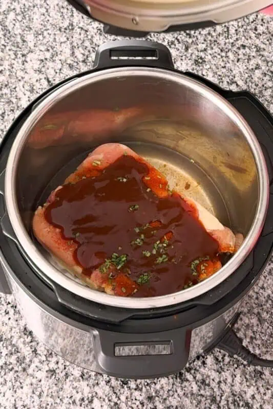 Frozen chicken thighs in instant pot covered in bbq sauce.