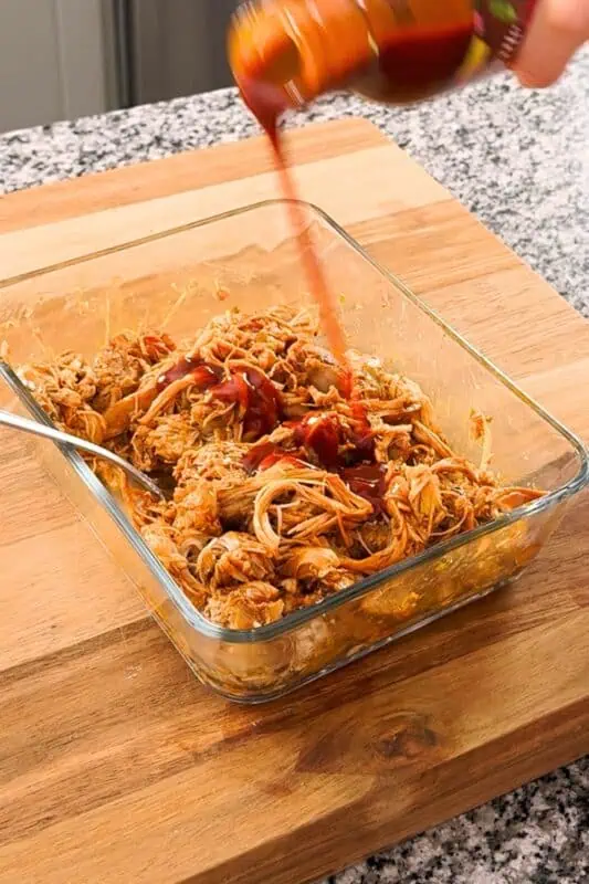 bbq sauce being poured over shredded chicken thighs.