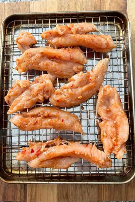 Raw chicken tenders coated in spicy sauce.