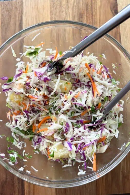 Pineapple slaw in glass bowl with tongs.