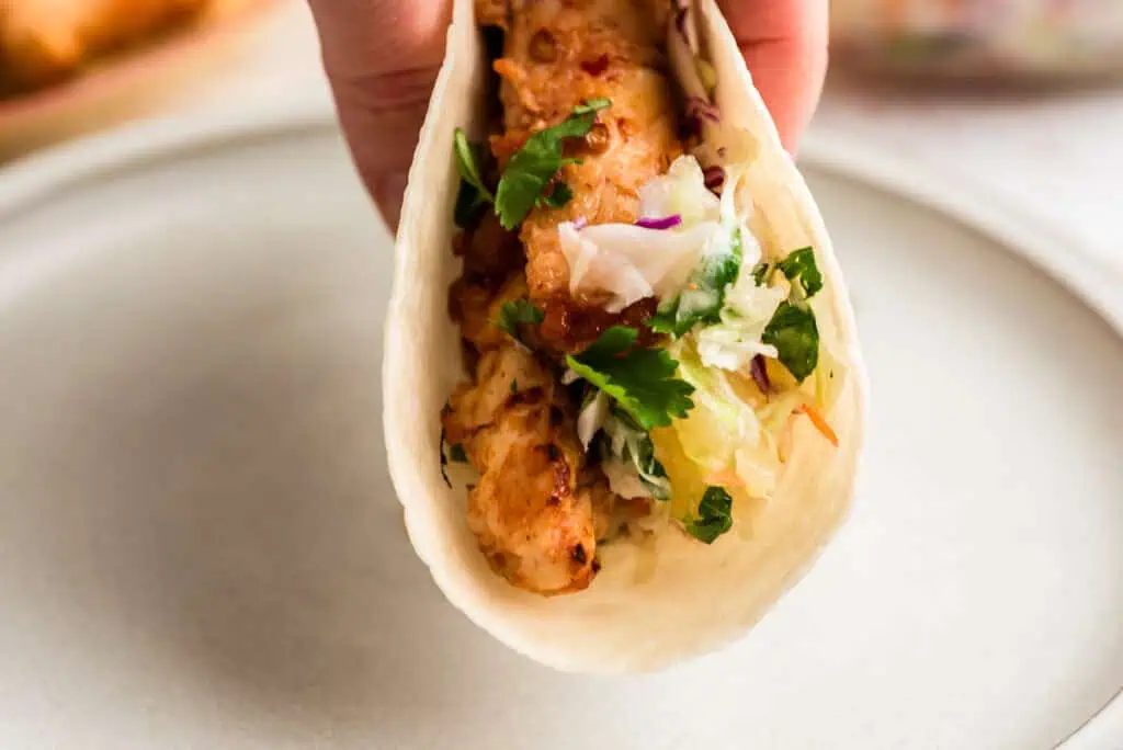 Hand picking up a single pineapple chipotle chicken taco.