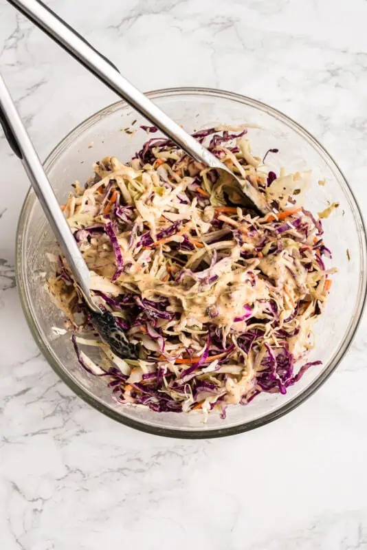 Blackening ranch dressing over slaw in a glass bowl.