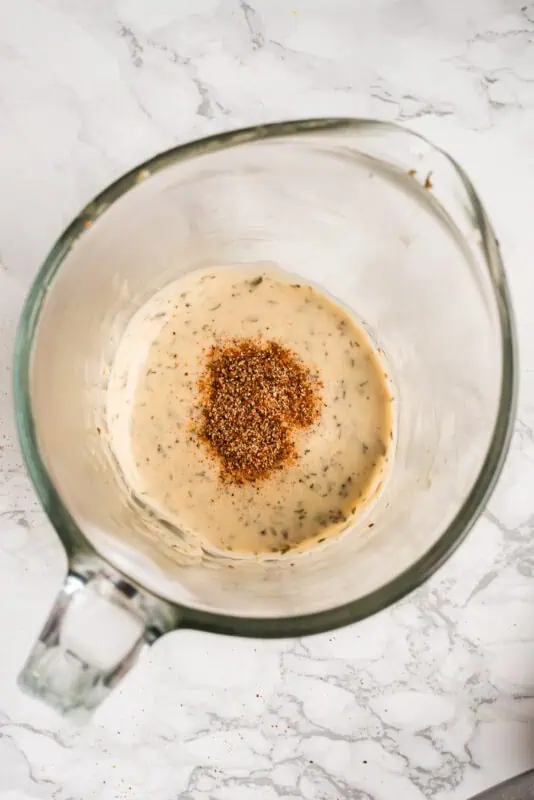 Blackening seasoning added to ranch dressing in a glass measuring cup.