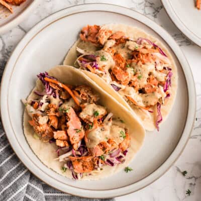 Two tacos with blackened salmon and slaw on a white plate.