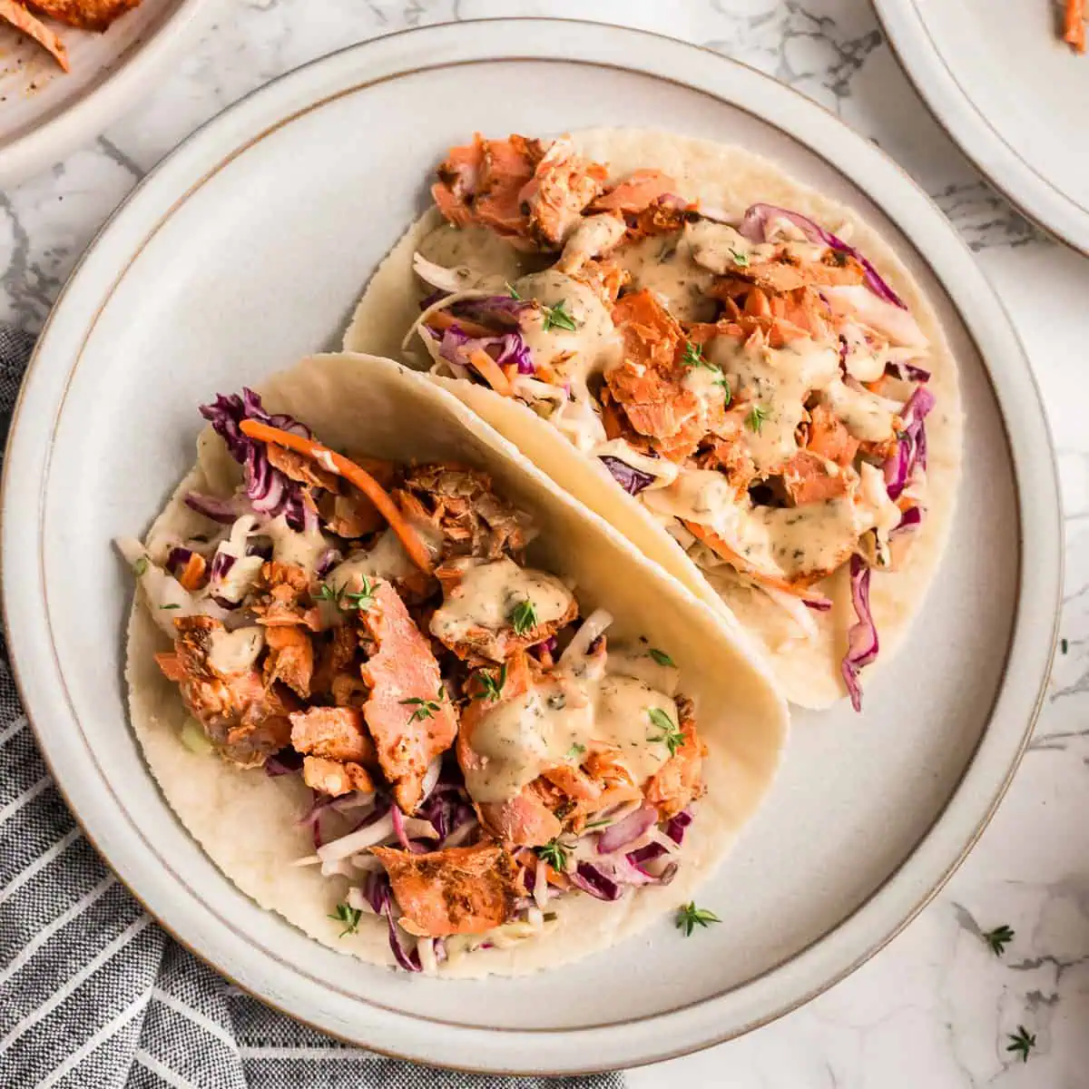 Two tacos with blackened salmon and slaw on a white plate.