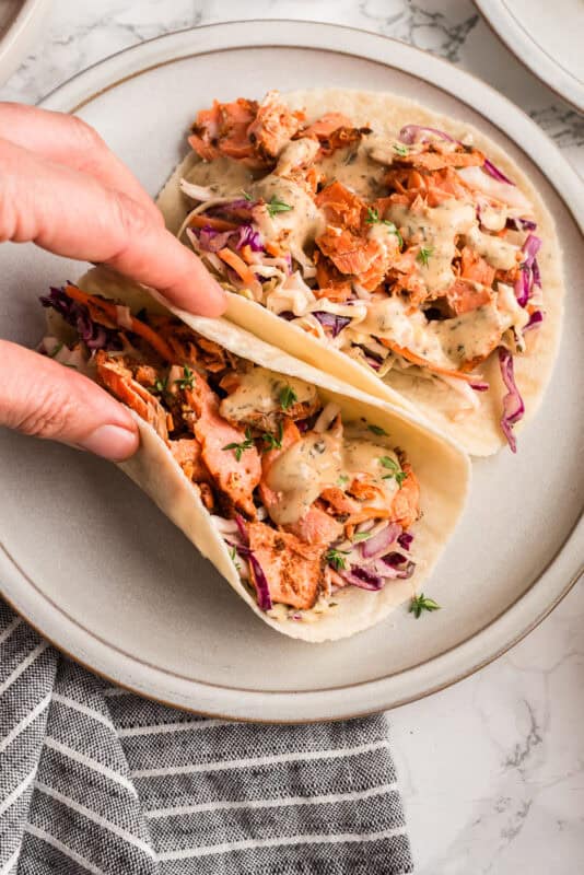 Hand folding a blackened salmon taco, lifting it from the plate.