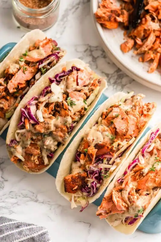 Four blackened salmon tacos being held by a taco holder.