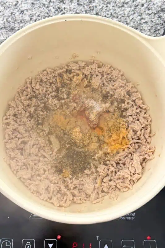 Spices and tomato paste added to cooked ground chicken in pot.