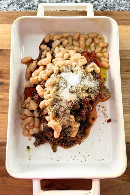 Casserole dish filled with tomatoes, white beans, spices.