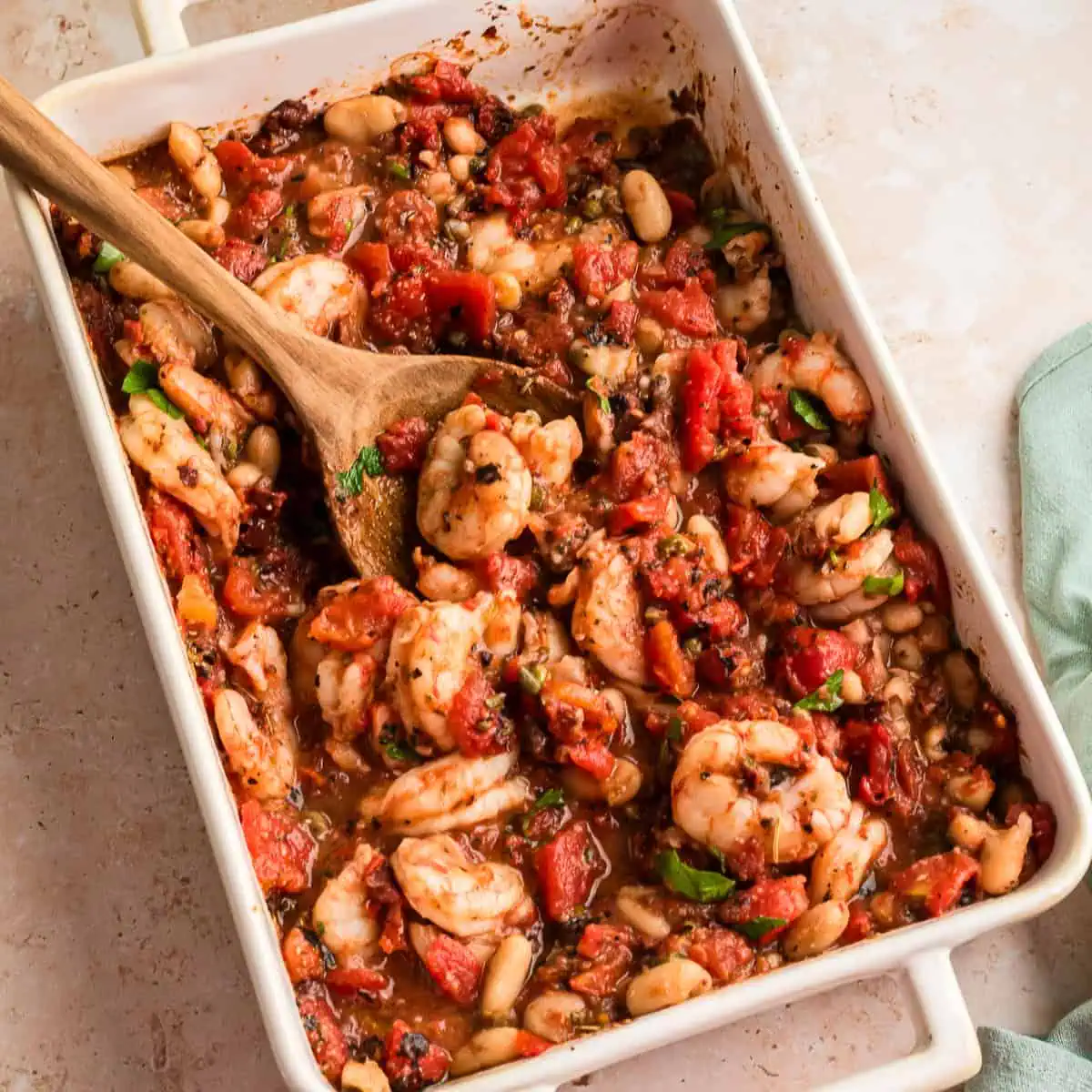 Casserole dish filled with Mediterranean Shrimp, spoon resting in the dish.