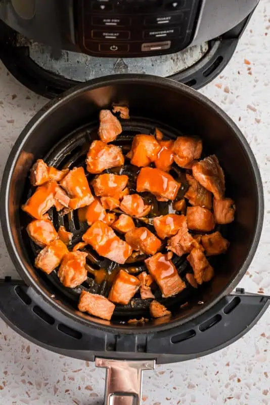 Buffalo sauce drizzled over cooked salmon bites in air fryer.