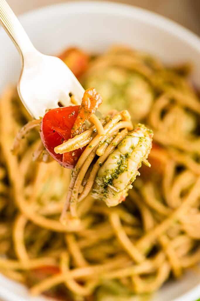 Fork holding pesto shrimp pasta over the bowl.