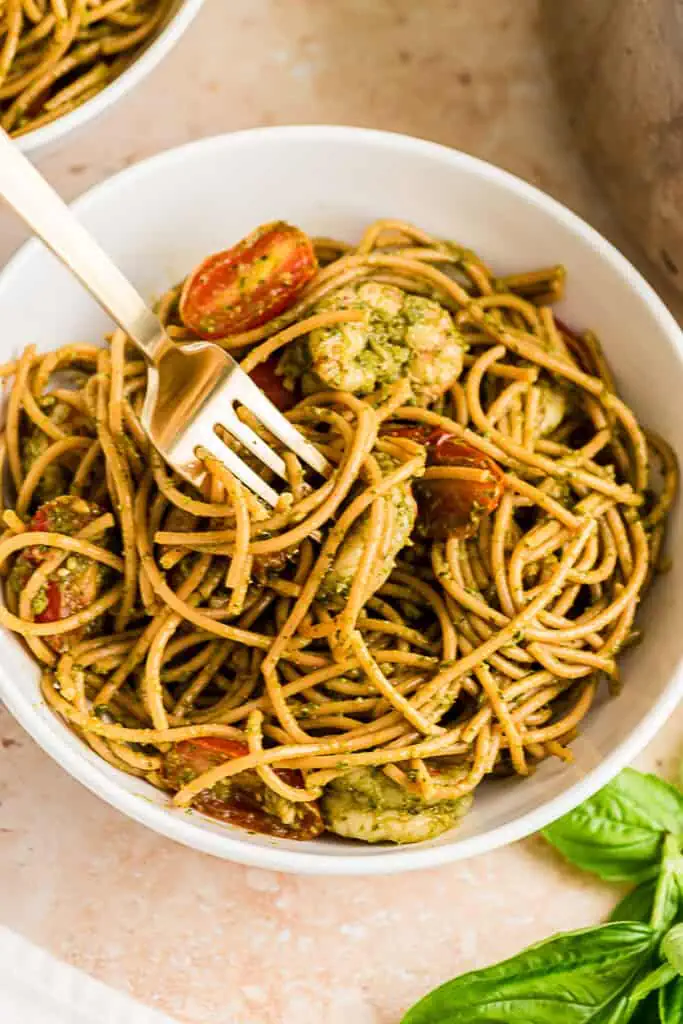 Fork resting in a bowl of pesto shrimp pasta.