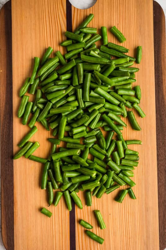 Green beans cut into bite size pieces on wood cutting board.