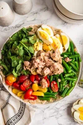 All the ingredients for niçoise tuna pasta salad in a white bowl before tossing.
