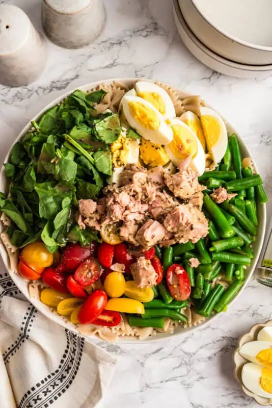 All the ingredients for niçoise tuna pasta salad in a white bowl before tossing.