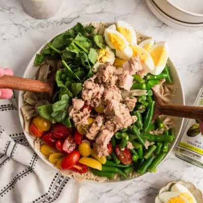 Two wood spoons tossing the Niçoise Tuna Pasta Salad.