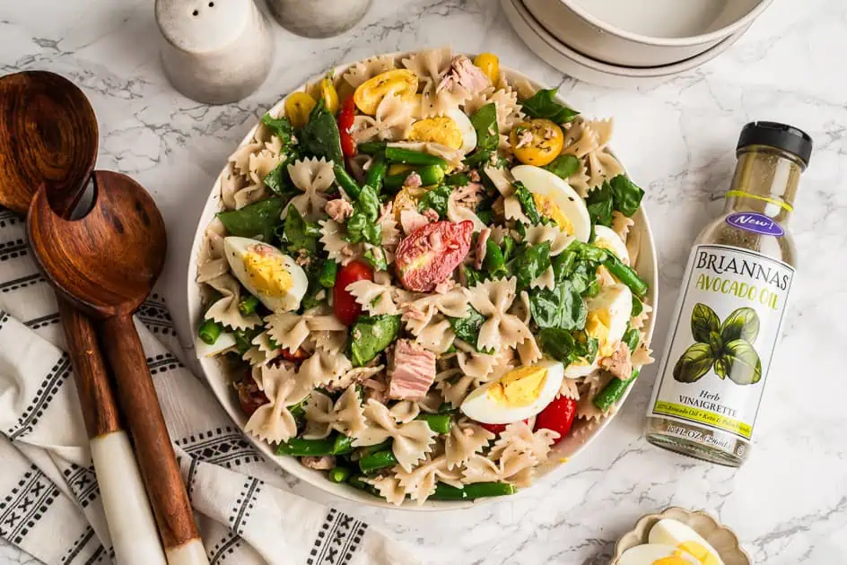 Niçoise tuna pasta salad in a white bowl, wood spoons on the side. 