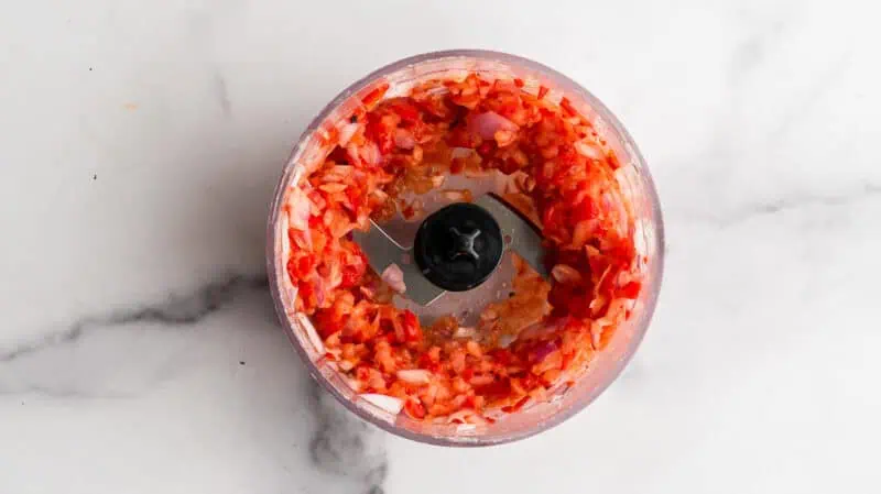 Small food processor filled with chopped red onion and peppers.