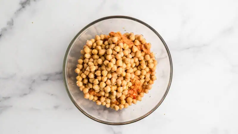Chickpeas added to large glass bowl with chickpea mixture.